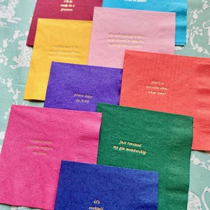 May include: A set of ten colourful napkins with gold lettering. Each napkin has a different saying, such as "I'll be comfy in a  princess", "That's a horrible idea. What time?", "Just renewed my gin membership", and "It's cocktail o'clock".