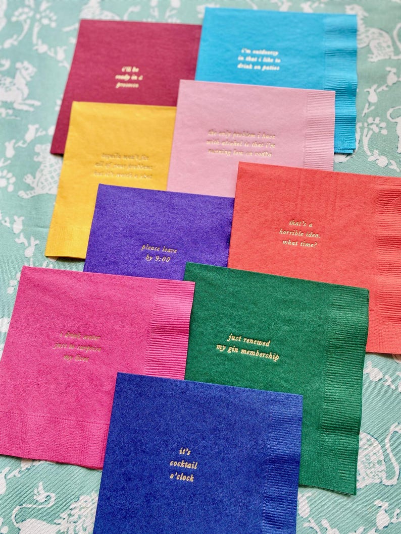 May include: A set of ten colourful napkins with gold lettering. Each napkin has a different saying, such as "I'll be comfy in a  princess", "That's a horrible idea. What time?", "Just renewed my gin membership", and "It's cocktail o'clock".