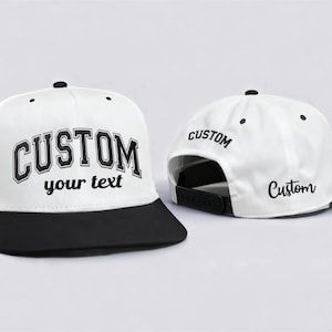 May include: White and black custom baseball cap. The front of the cap features the word "CUSTOM" in a bold, black, collegiate-style font, with "your text" below. The back of the cap has "CUSTOM" printed on it.