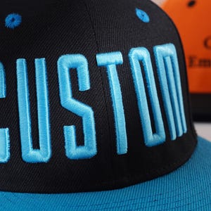 May include: A black and blue baseball cap with the word "CUSTOM" embroidered in blue on the front.