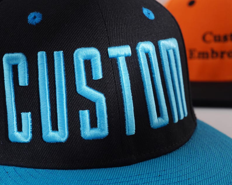 May include: A black and blue baseball cap with the word "CUSTOM" embroidered in blue on the front.