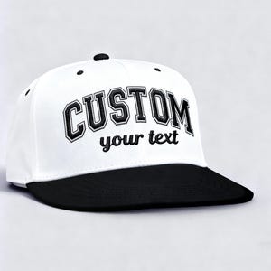 May include: A white and black baseball cap with the word "CUSTOM" embroidered in black, arched across the front. The text "your text" is embroidered below. The cap has a flat brim and a button on top.