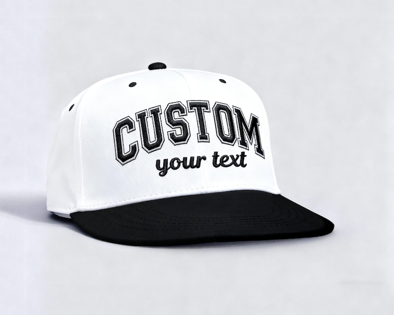 May include: A white and black baseball cap with the word "CUSTOM" embroidered in black, arched across the front. The text "your text" is embroidered below. The cap has a flat brim and a button on top.