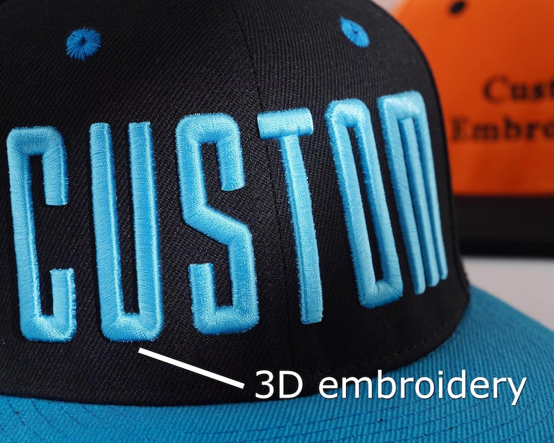 May include: Black and blue baseball cap with "CUSTOM" embroidered in light blue 3D lettering. The cap features a flat brim and a matching blue top button. The text "3D embroidery" is also visible.