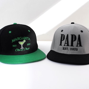 May include: Two black and green baseball caps with embroidered text. One cap says "Margarita Est. 2025 Clever Club" with a green margarita glass graphic. The other cap says "Papa Est. 2025".