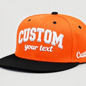 May include: An orange and black custom baseball cap. The cap features the word "CUSTOM" in white, outlined in a collegiate font, with the words "your text" below. The brim is black, and the word "Custom" is on the side.