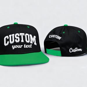 May include: Black and green custom baseball cap with the word "CUSTOM" in white block letters on the front. The cap has a green brim and a green button on top. The back of the cap also has the word "CUSTOM" in white.
