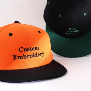 May include: A bright orange baseball cap with a black brim. The front of the cap has black embroidery that reads "Custom Embroidery".