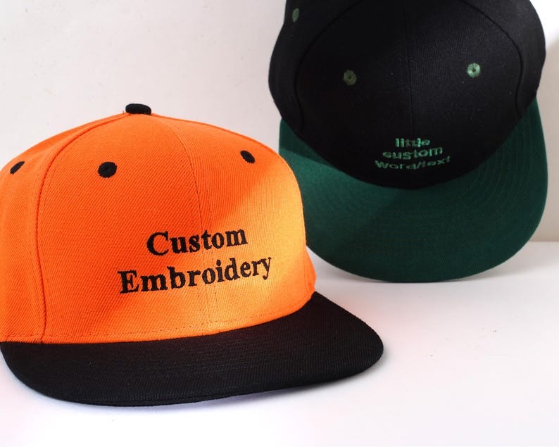 May include: A bright orange baseball cap with a black brim. The front of the cap has black embroidery that reads "Custom Embroidery".