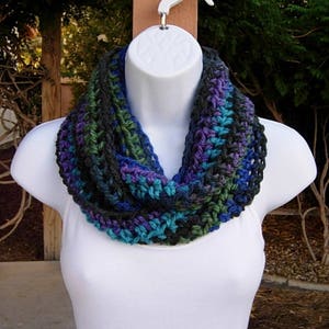 May include: A crocheted infinity scarf in shades of teal, purple, and black. The scarf is made with a simple stitch pattern and has a relaxed, drapey feel.