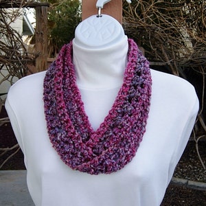 May include: A crocheted infinity scarf in shades of pink and purple. The scarf is made with a chunky yarn and has a simple, elegant design.