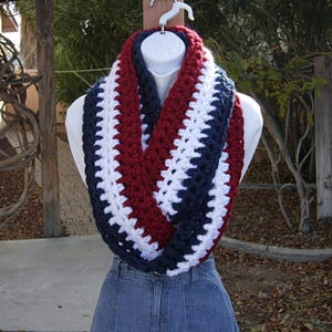 以下が含まれることがあります： 赤、白、青のクロシェの無限スカーフ。スカーフは太い糸で作られており、シンプルなストライプ柄です。