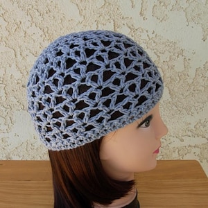 May include: A pale blue crochet hat with an open, lacy pattern. The hat is made from soft yarn and has a rounded shape. The hat is displayed on a mannequin head.