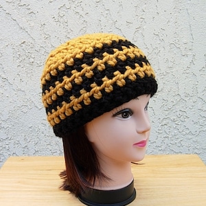 May include: A black and gold crocheted beanie hat. The hat is made with a simple stitch pattern and has a slouchy fit.