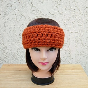 May include: A crocheted headband in a burnt orange color. The headband is wide and has a simple, textured design.