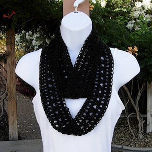 May include: A black crocheted infinity scarf with a delicate openwork pattern. The scarf is displayed on a white mannequin.