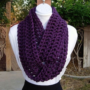 May include: A purple crocheted infinity scarf. The scarf is made with a simple stitch pattern and has a soft, drapey texture.