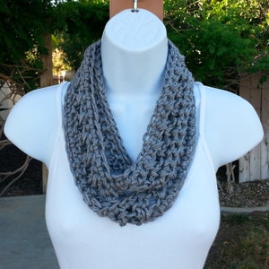 May include: A gray crocheted infinity scarf. The scarf is made with a simple stitch pattern and is a great accessory for any outfit.