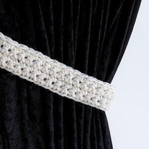 May include: A white crocheted curtain tieback with a simple design, tied around black velvet curtains.