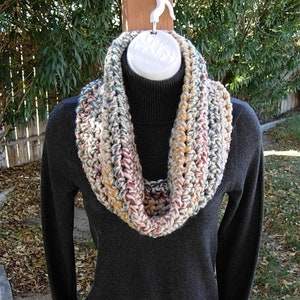 May include: A crocheted infinity scarf in a multi-coloured pattern of cream, brown, red, and green.