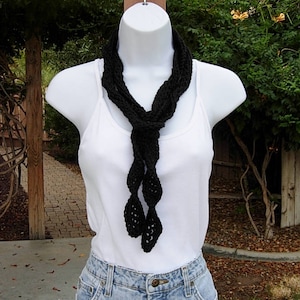 May include: A black crocheted scarf with a knotted design. The scarf is worn around the neck of a mannequin.
