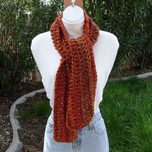May include: A crocheted scarf in shades of orange and brown. The scarf is made with a lacy stitch pattern and has a slightly textured look.