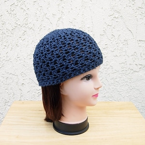 May include: A navy blue crocheted beanie hat with a loose, open weave pattern. The hat is shown on a mannequin head with brown hair.
