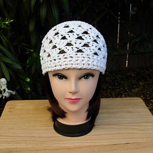 May include: White crocheted beanie hat with a geometric pattern. The hat is made with a lightweight yarn and has a comfortable fit.