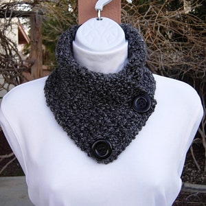 May include: A gray knitted cowl neck scarf with two black buttons. The scarf is on a white mannequin.