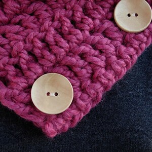 May include: A close-up of a pink knitted scarf with two wooden buttons. The buttons have a single hole in the center.