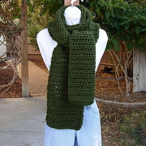 May include: A dark green crocheted scarf with a simple stitch pattern. The scarf is displayed on a mannequin wearing a white shirt and blue jeans.