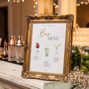 Könnte beinhalten: Ein goldgerahmtes Bar-Menü mit Cocktail-Illustrationen und Rezepten. Das Menü zeigt drei Cocktails: Wild Berry, Mojito und Margarita. Der Rahmen steht auf einer weißen Theke mit Cocktail-Shakern und Gläsern mit Zutaten.