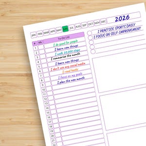 May include: A white 2026 planner page with a to-do list and self-improvement goals. The planner includes a list of tasks such as "I do good for people" and "I read books". The page is on a wooden surface.