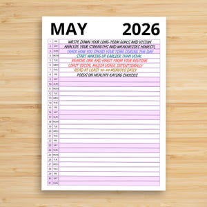 Puede incluir: Un calendario blanco de mayo de 2026 con fondo de madera. El calendario incluye entradas diarias con indicaciones como "Escribe tus metas y visión a largo plazo" y "Concéntrate en opciones de alimentación saludable."