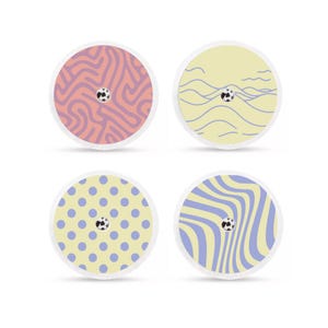 Op de afbeelding: Vier ronde zelfklevende pleisters met verschillende patronen. Eén heeft een roze en paars abstract ontwerp, een andere heeft blauwe golvende lijnen op een gele achtergrond, een derde heeft blauwe stippen op een gele achtergrond en de laatste heeft blauwe golvende lijnen op een gele achtergrond.