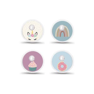 May include: Four circular medical device covers with decorative designs. One features a unicorn face, another a rainbow, a third a cupcake, and the last a pink donut. Each has a small, silver-coloured centre.