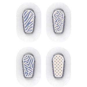 Op de afbeelding: Vier pleisters voor medische apparaten met decoratieve ontwerpen. De patronen omvatten een blauw-witte zebra streep, een luipaardprint, een blauw-wit abstract ontwerp en een beige stippenpatroon. Elke pleister is op een witte, ovaalvormige lijm geplaatst.
