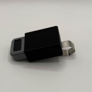 May include: A black and gray key holder with a metal clip. The key holder has a textured surface and a black rubber cover.