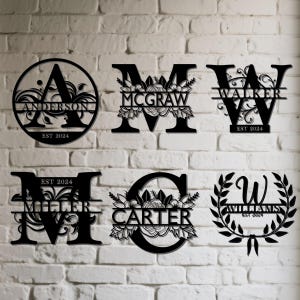 May include: Black metal family name signs with decorative floral and leaf accents. Each sign features a different letter, family name, and the year "EST 2024". The signs are displayed against a white brick wall.