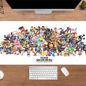 Könnte beinhalten: Eine weiße, rechteckige Schreibtischunterlage mit einer farbenfrohen Collage von Charakteren aus dem Videospiel Super Smash Bros. Ultimate. Das Logo des Spiels befindet sich unten. Eine Tastatur, eine Maus und eine Kaffeetasse sind ebenfalls zu sehen.