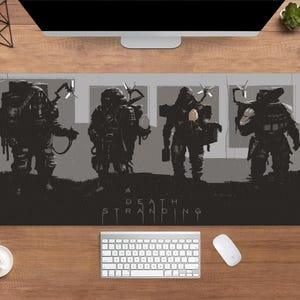 May include: A rectangular desk mat featuring a gray and black illustration of four figures in futuristic armor. The words "DEATH STRANDING" are printed in white at the bottom. A keyboard, mouse, and coffee cup are visible.
