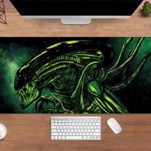 Puede incluir: Alfombrilla de ratón rectangular con una ilustración detallada de una criatura Alien en tonos verdes y negros sobre un fondo oscuro con temática espacial. También se ven un teclado, un ratón y una taza de café.