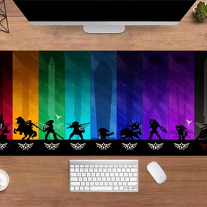 May include: A rectangular desk mat featuring a colorful gradient background with black silhouettes of characters and swords. The bottom edge has a repeating white and black design. A keyboard, mouse, and coffee cup are visible.
