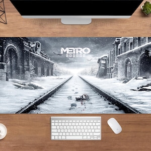 May include: A rectangular desk mat featuring a snowy landscape with train tracks and buildings. The mat has the words "METRO EXODUS" in white. A keyboard, mouse, and coffee cup are visible on the wooden desk.