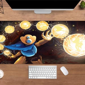 Puede incluir: Alfombrilla de ratón rectangular con un personaje de dibujos animados con una capa azul y un brazo dorado, rodeado de orbes brillantes. El fondo es oscuro con grietas en forma de relámpago. Un teclado y un ratón blancos están debajo.