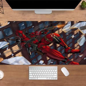 May include: A rectangular desk mat featuring a dynamic illustration of Deadpool in a red and black suit, firing guns amidst shattered glass. The design includes a detailed depiction of the character and a background of a building facade.