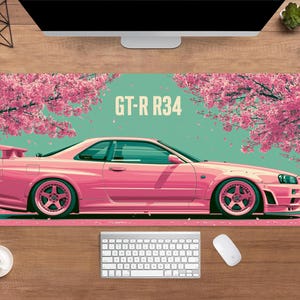 May include: Pink GT-R R34 car illustration on a mousepad. The car is set against a backdrop of pink cherry blossom trees and a teal background. The mousepad also has a white keyboard and mouse.