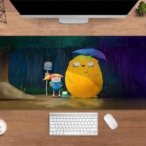 May include: A rectangular desk mat featuring a cartoon scene with a large yellow character holding a blue umbrella, and a smaller character with a red and yellow umbrella. The background shows a rainy forest scene with a bus stop.