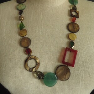 May include: A long necklace made of brown, green, and red beads. The beads are various shapes, including circles and squares.