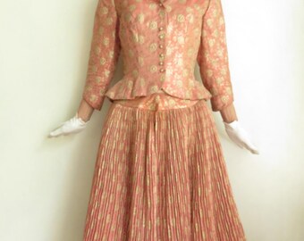 May include: A pink and gold brocade dress with a fitted bodice and a full skirt. The dress has a sweetheart neckline and a button closure at the front. The skirt is pleated and has a wide waistband.